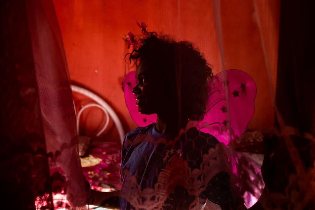 A girl with curly hair is behind a red curtain